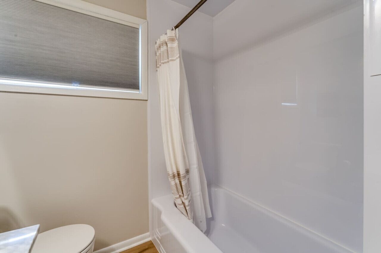 Une salle de bain avec une baignoire, des toilettes et une fenêtre avec des stores.