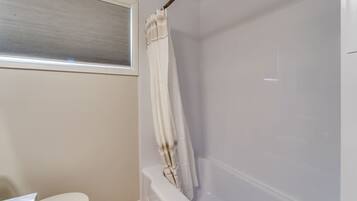 Une salle de bain avec une baignoire, des toilettes et une fenêtre avec des stores.
