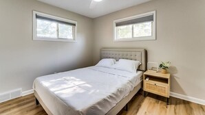 Een slaapkamer met een bed, nachtkastje en plafondventilator. Er zitten ramen in de muren.