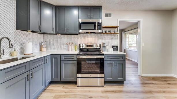 Een moderne keuken met grijze kastjes, roestvrijstalen apparatuur en een backsplash met een herringbone patroon.