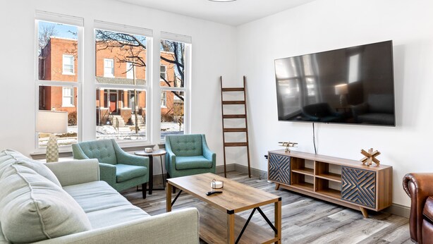 A modern living room with a large TV, teal armchairs, a wooden coffee table, and a wooden cabinet.