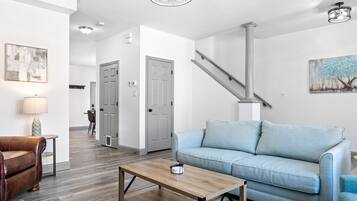 A modern living room with a light blue sofa, a wooden coffee table, and a brown leather chair. A staircase is visible in the background.