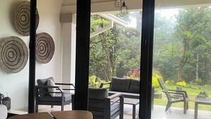 A modern living room with a large sliding glass door leading to a lush garden. - Casa de Verano in Valle Bonito

 (Provincia de Panamá Oeste)