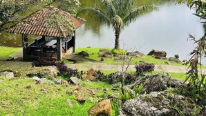 A gazebo with a tiled roof overlooking a pond, surrounded by lush greenery and hills. - Casa de Verano in Valle Bonito

 (Provincia de Panamá Oeste)