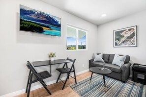 Ein modernes Wohnzimmer mit Essbereich, einem grauen Sofa und einem großen Fenster.