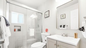 Ein modernes Badezimmer mit einer gläsernen Duschkabine, einer weißen Toilette und einem Waschbecken mit Spiegel darüber.