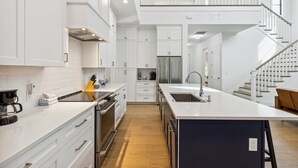 Een moderne keuken met witte kasten, een groot eiland, roestvrijstalen apparatuur en een houten trap.