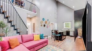 Una sala de estar moderna con un sofá rosa, una escalera, un comedor y una cocina.