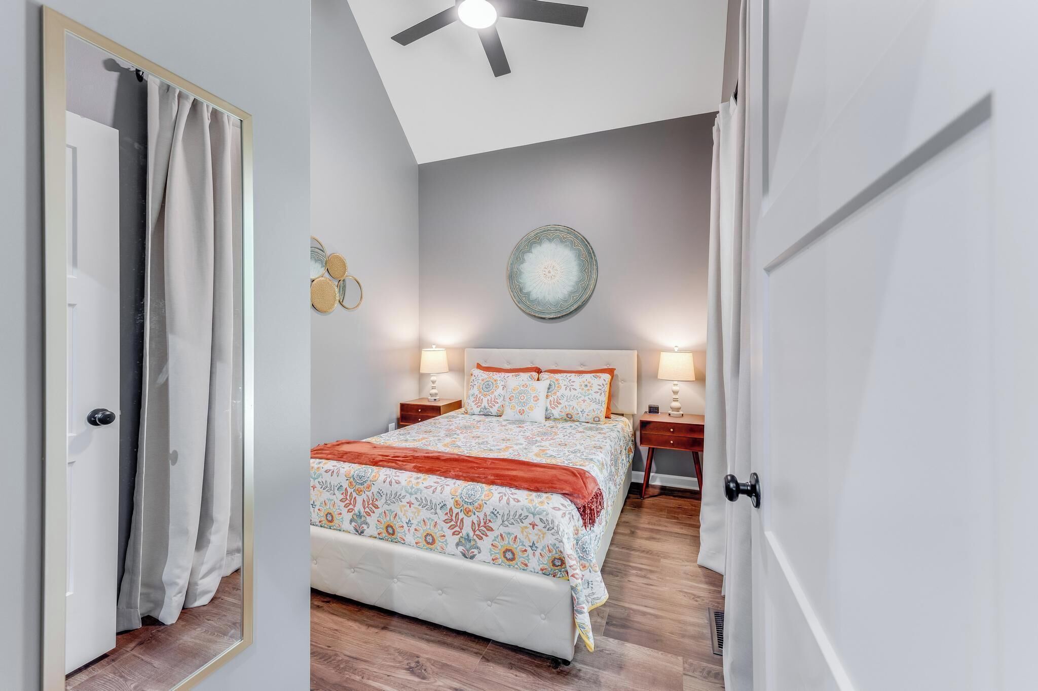 A bedroom with a bed, bedside tables, a ceiling fan, and a decorative plate on the wall.