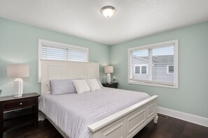 A bedroom with a large bed, two bedside tables, and a window with blinds.