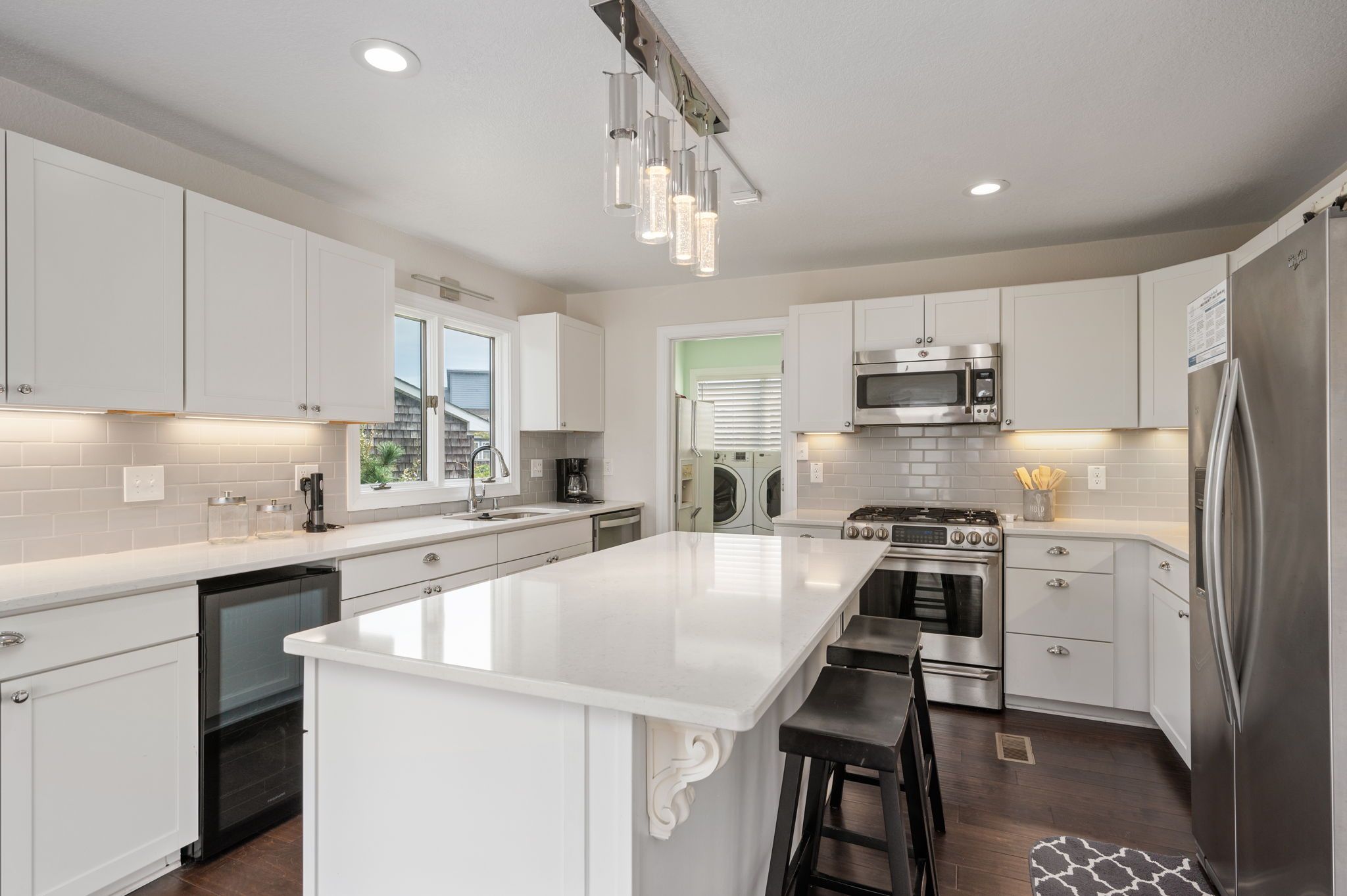 A modern kitchen with white cabinetry, stainless steel appliances, and a central island with bar stools.