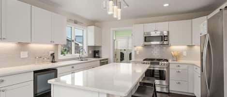 A modern kitchen with white cabinetry, stainless steel appliances, and a central island with bar stools.