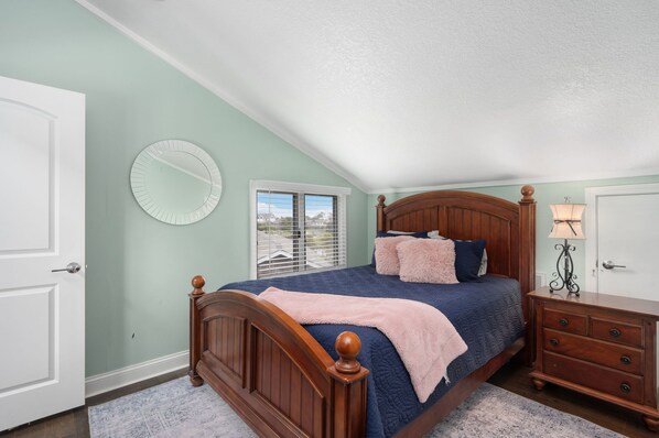 Quarto com cama de madeira, mesa de cabeceira, abajur e janela com persianas.