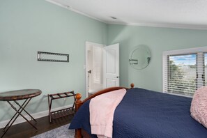 A bedroom with a bed, a round mirror, a small table, and a door. - ONHC21D: Soundfront, Private Boat Dock, Sunset Views! (Nags Head)