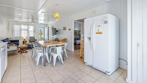 A spacious kitchen with white cabinetry, a large refrigerator, and a dining area with white chairs and a wooden table. - Lunar Tide: Pet Friendly, Oceanside, Close to Beach and Avalon Pier (Kill Devil Hills)
