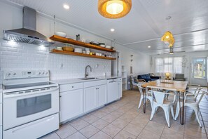 A modern kitchen with white cabinetry, a built-in oven, and a dining area with white chairs and a wooden table.