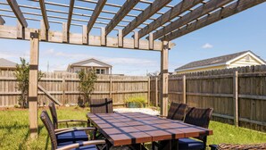 Une structure en bois formant une pergola, avec une table de pique-nique et des chaises, installée dans un jardin.