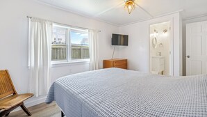 Une chambre à coucher avec un grand lit, un banc en bois, un téléviseur fixé au mur et une fenêtre avec des rideaux.