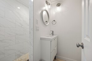A bathroom with white marble tiles, a white sink with a mirror above it, and a door with a silver handle.