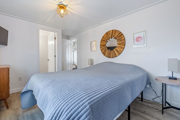 A bedroom with a large bed, a round wall clock, and a small bedside table with a lamp.