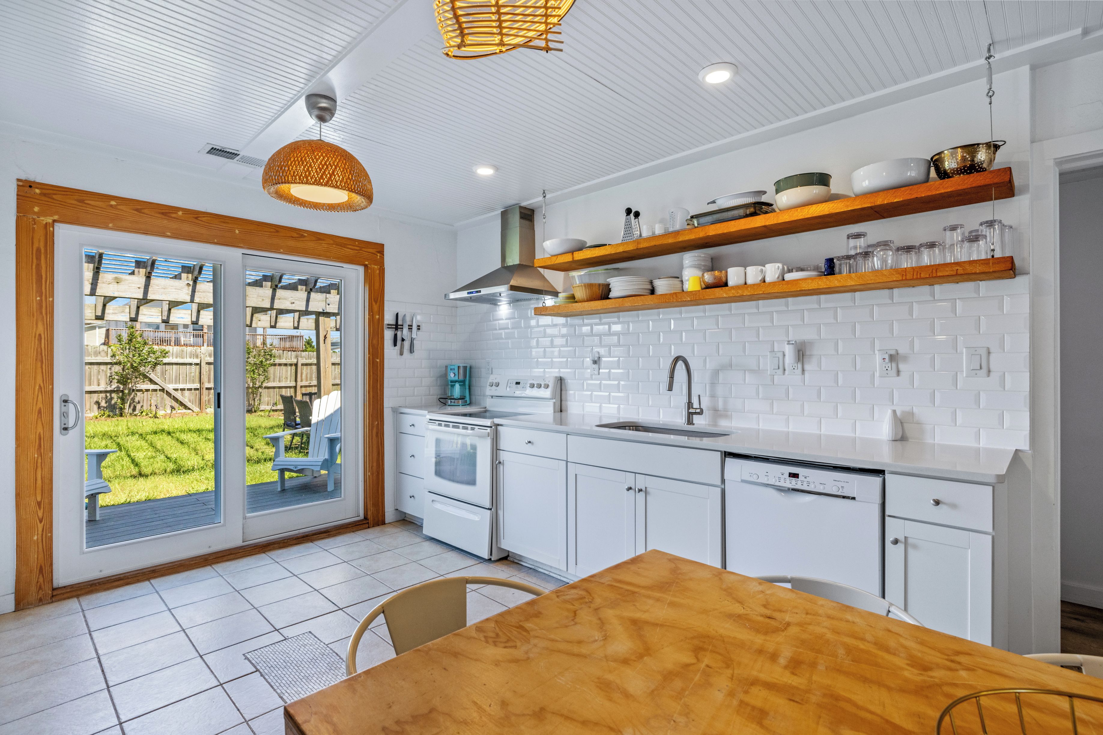 A modern kitchen with white cabinets, wooden shelves, and a dining area with a wooden table and chairs.