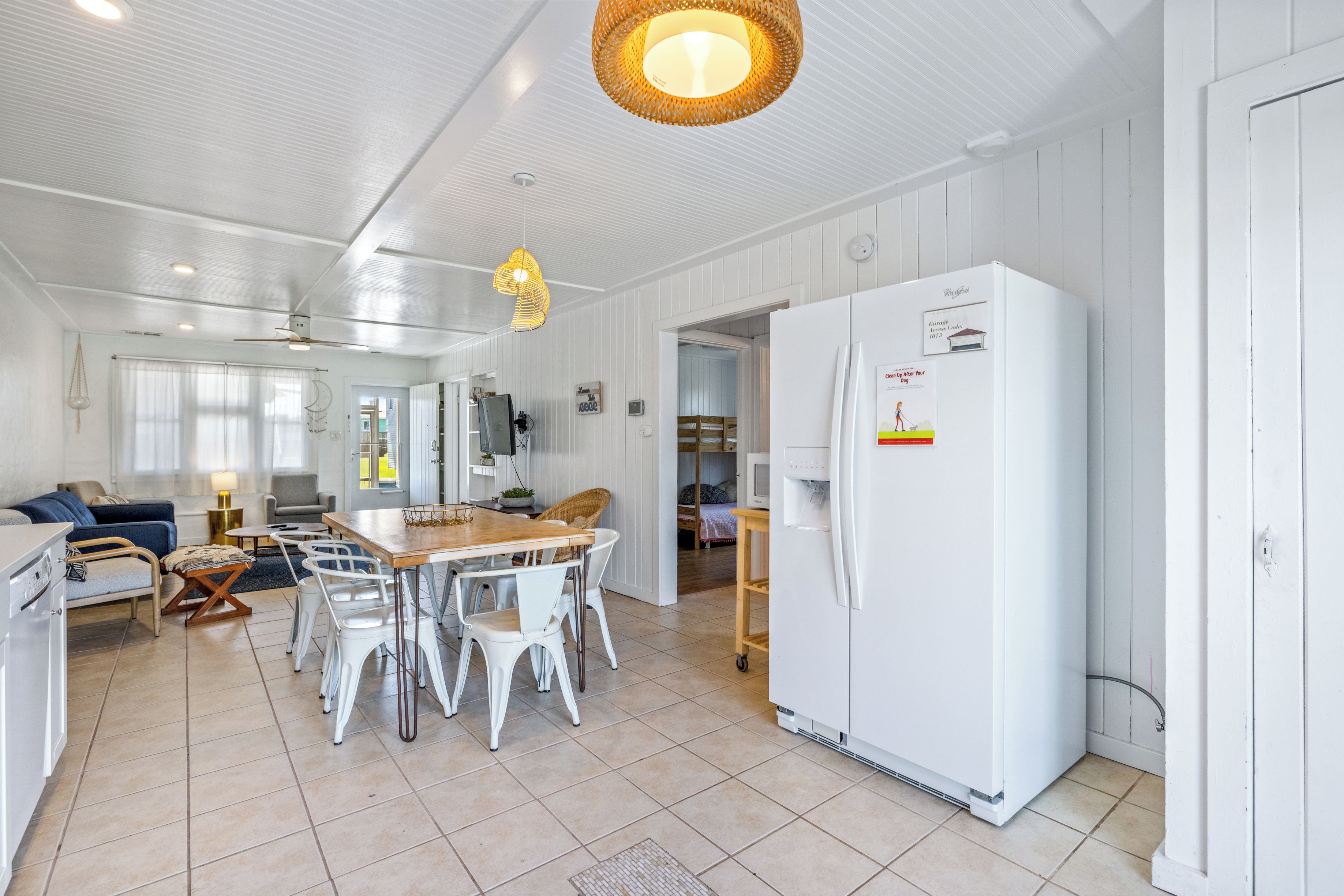 A spacious kitchen with white cabinetry, a large refrigerator, and a dining area with white chairs and a wooden table.