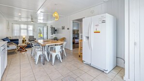 Une cuisine spacieuse avec des meubles blancs, un grand réfrigérateur et un coin repas comprenant des chaises blanches et une table en bois.