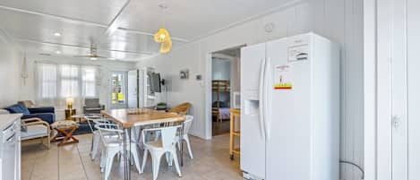 A spacious kitchen with white cabinetry, a large refrigerator, and a dining area with white chairs and a wooden table.