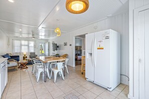 A spacious kitchen with white cabinetry, a large refrigerator, and a dining area with white chairs and a wooden table.