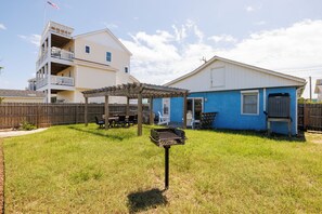 A backyard with a grill, a wooden pergola, and a blue house.