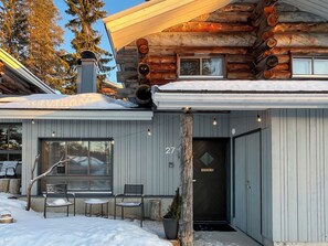 Une cabane en rondins dotée d’un espace extérieur couvert avec des sièges, d’une grande fenêtre et d’une porte portant le numéro 27.