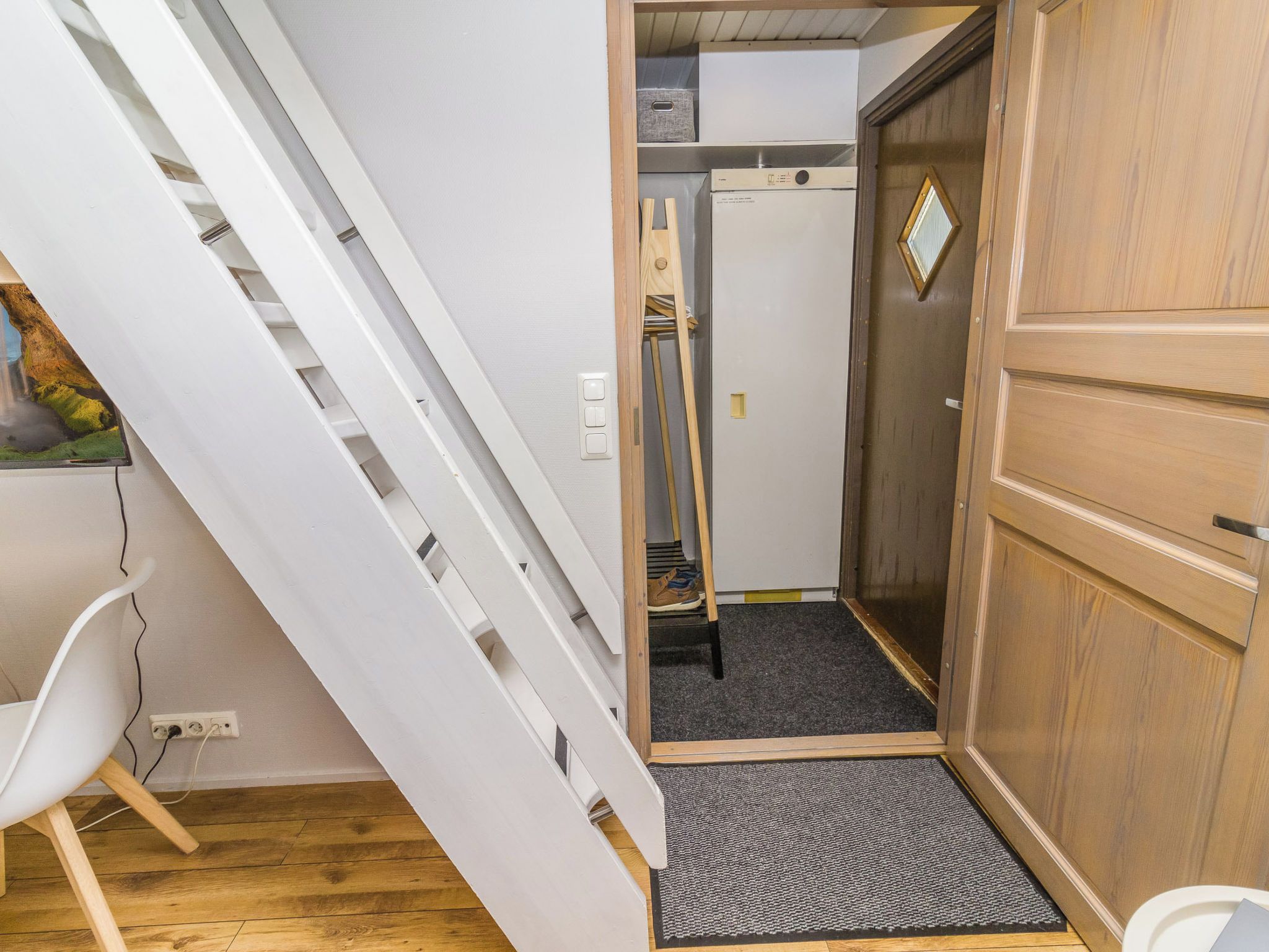 Ein kompakter Raum mit einem Holzschrank, einem weißen Stuhl, einem kleinen Schreibtisch und einem weißen Schrank mit Spiegel.