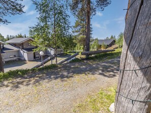 A gravel driveway leading to a wooden cabin with a metal gate, surrounded by trees and a clear sky. - Rukaköngäs 27 by Interhome (Kuusamo)