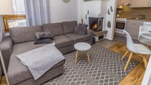 A modern living room with a sofa, a small round table, a fireplace, and a kitchen area. - Rukaköngäs 27 by Interhome (Kuusamo)