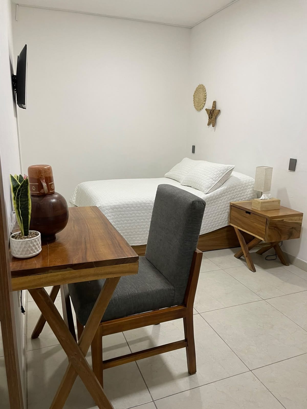 A bedroom with a bed, bedside table, lamp, and a small wooden nightstand.