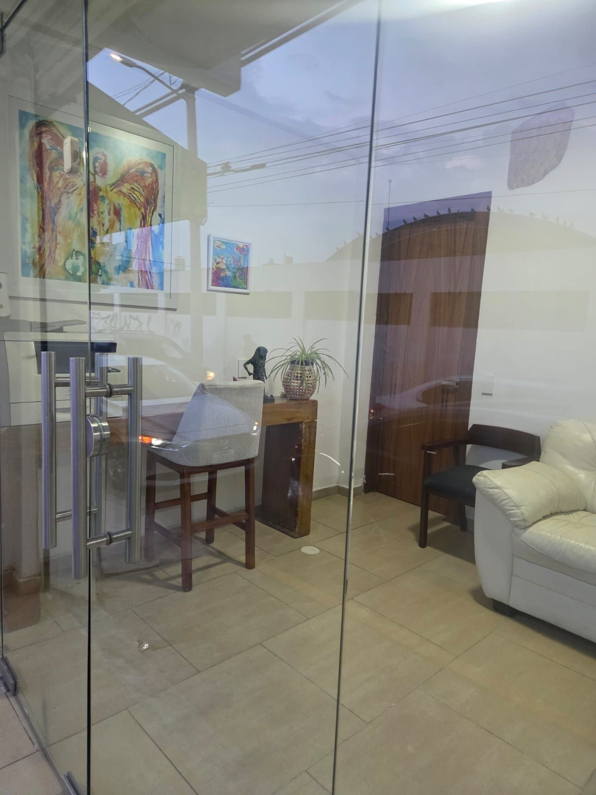 A modern interior with a glass partition, a dining area with a chair and table, a white sofa, and a potted plant.