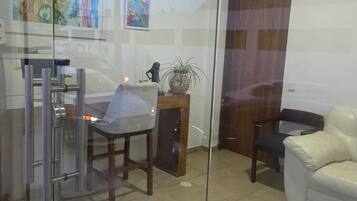 A modern interior with a glass partition, a dining area with a chair and table, a white sofa, and a potted plant.