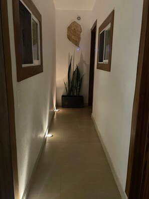 Un pasillo con una planta en maceta, un respiradero en el techo y una puerta al final.