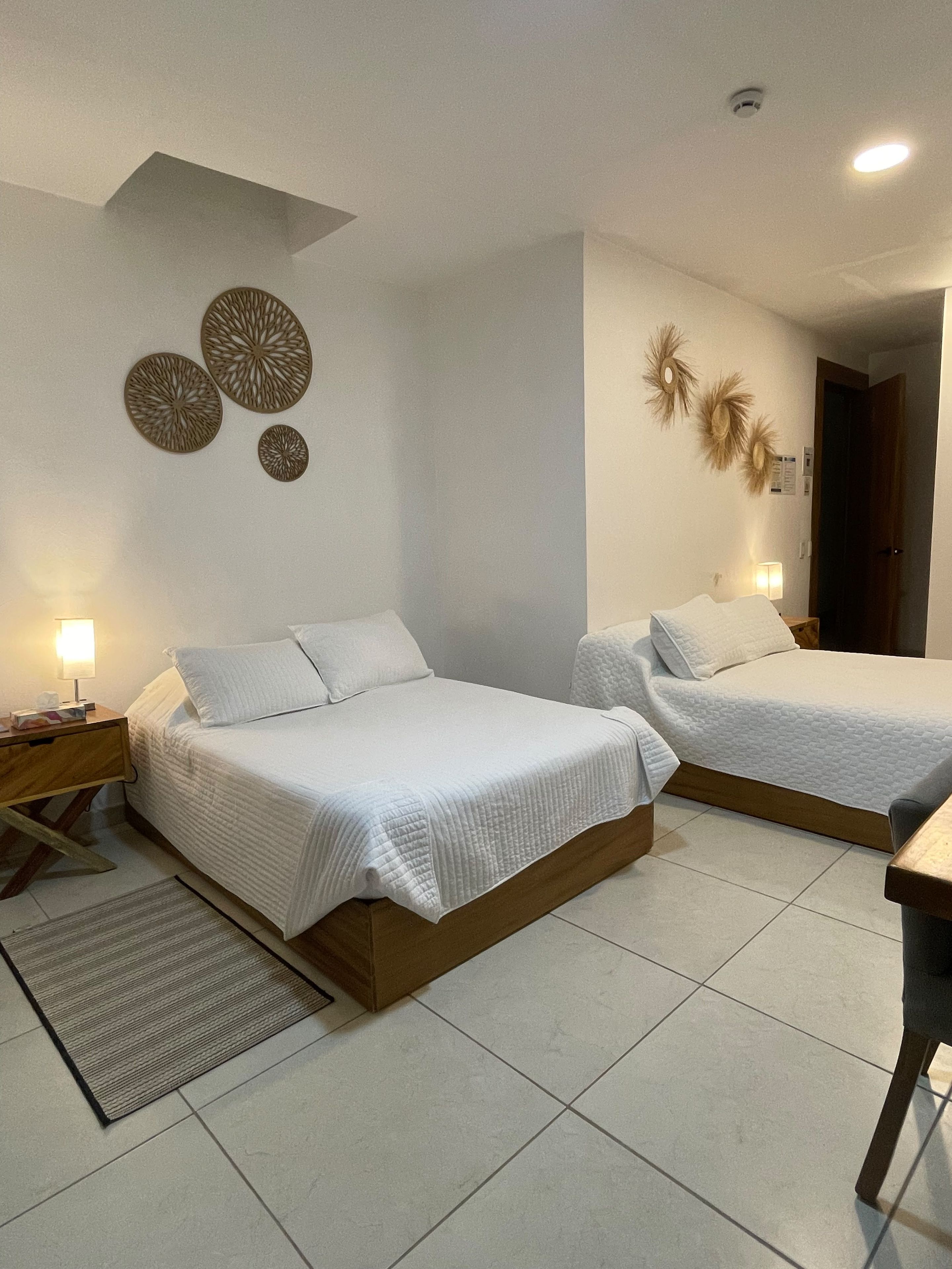 A bedroom with two beds, a bedside table with a lamp, and decorative wall art.