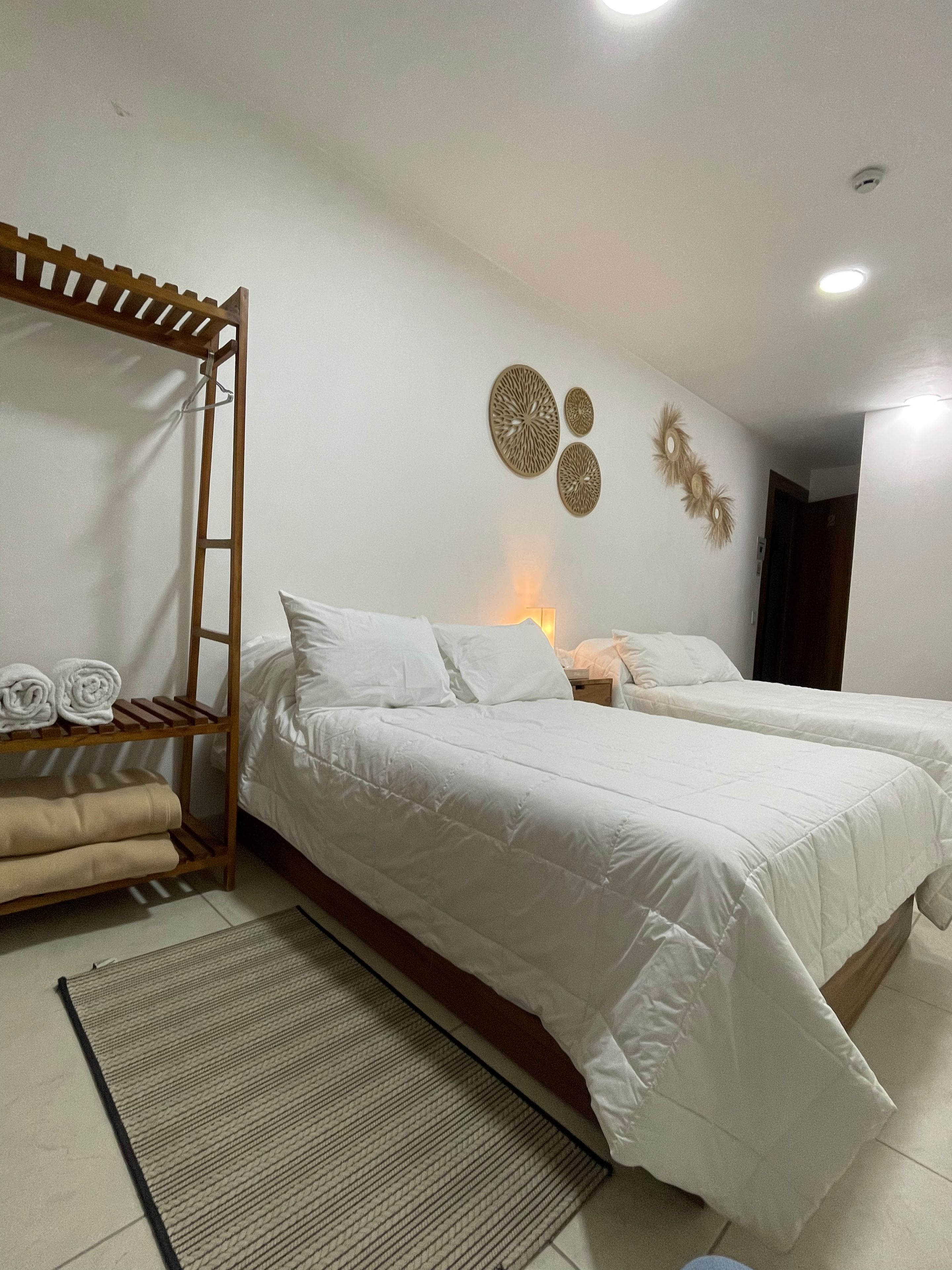 A bedroom with two beds, a wooden shelf with towels, and decorative wall art.