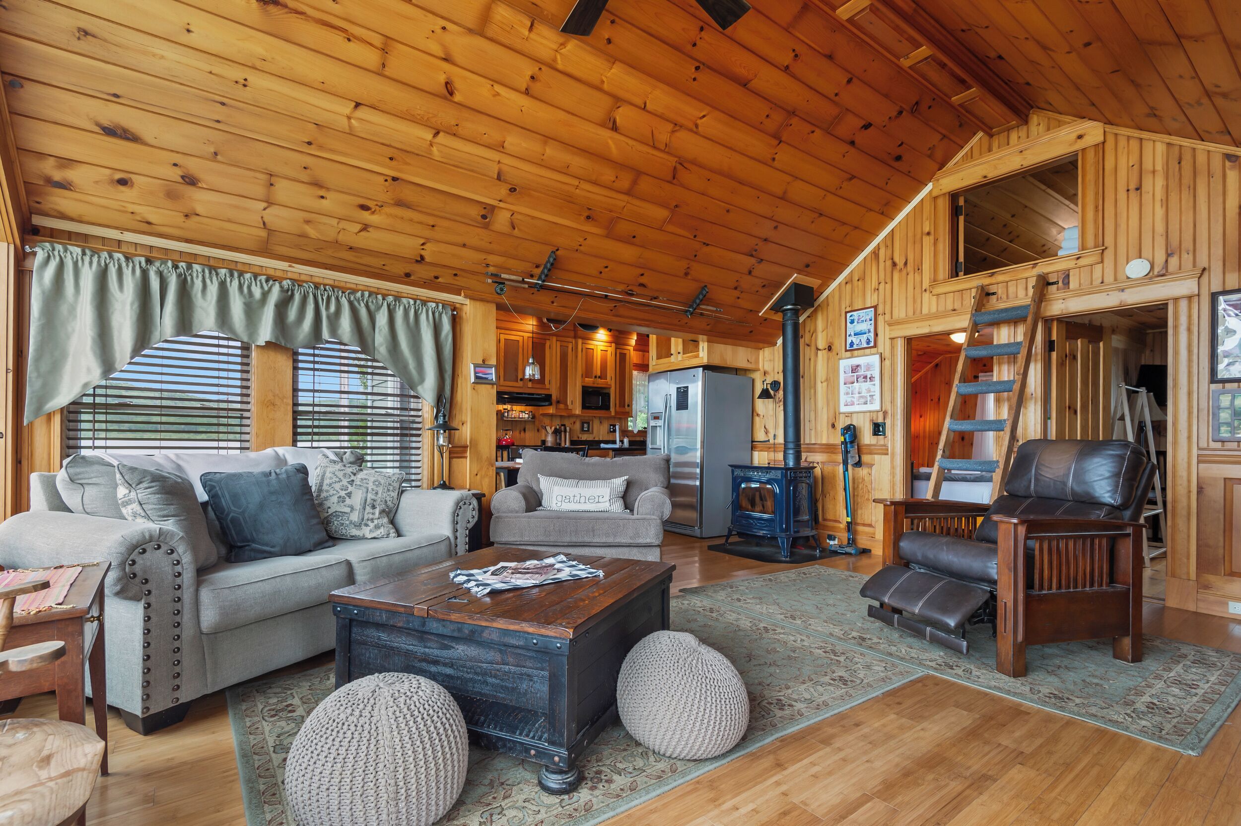 A cozy cabin interior with a wooden ceiling, a living room with a sofa, a coffee table, and a fireplace.
