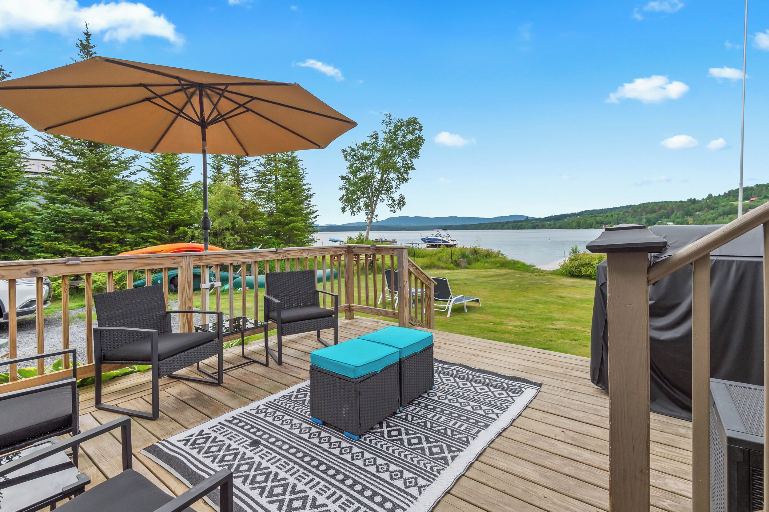 A deck with outdoor furniture, a large umbrella, and a view of a lake.