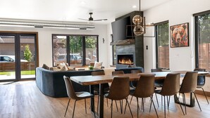 Ein moderner Essbereich mit Holztisch und -stühlen, einem integrierten Kamin und einem großen Fenster mit Blick ins Freie.