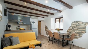 Un saló modern amb un sofà groc, una taula de dinar amb cadires i una cuina al fons.