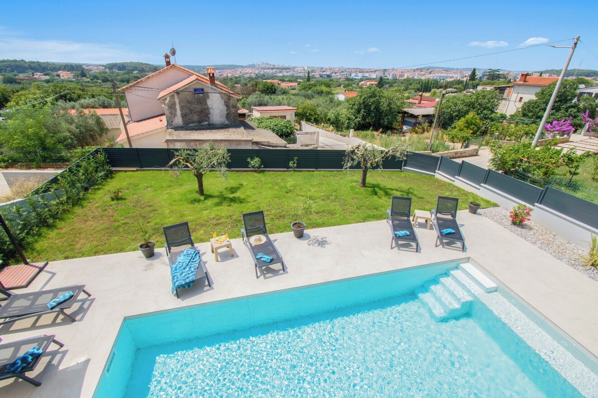 A swimming pool with lounge chairs and a grassy area with a view of a cityscape.