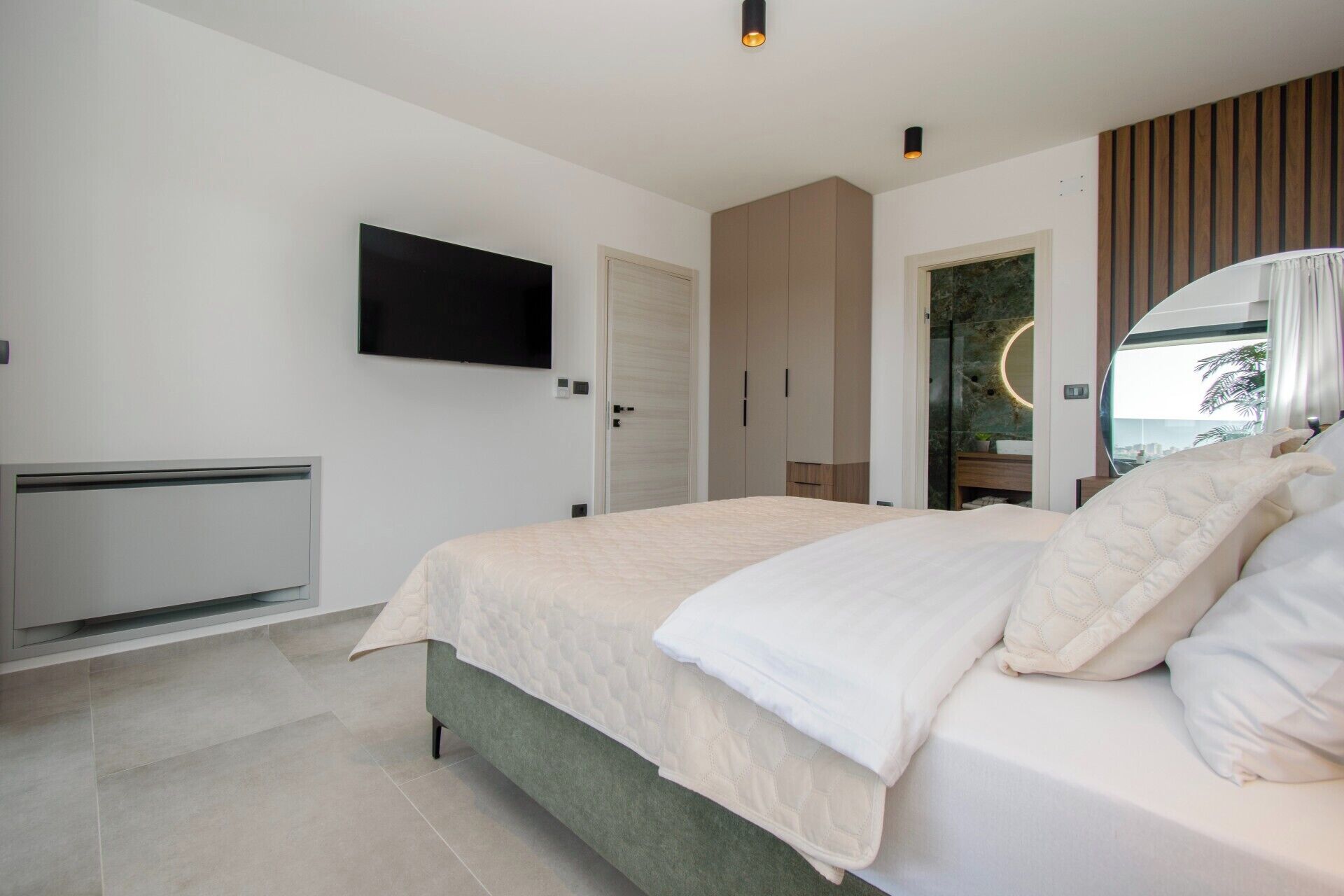 A modern bedroom with a large bed, a flat-screen TV mounted on the wall, and a walk-in closet with sliding doors.
