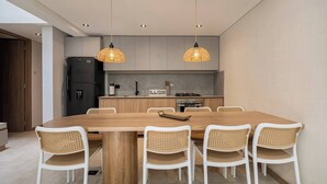 Eine moderne Küche mit einem Holztisch, sechs Korbstühlen, zwei Pendelleuchten und einem schwarzen Kühlschrank.