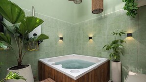 Ein Wellnessraum mit einer Holzwanne, Wandverkleidung mit grünem Muster und Topfpflanzen.