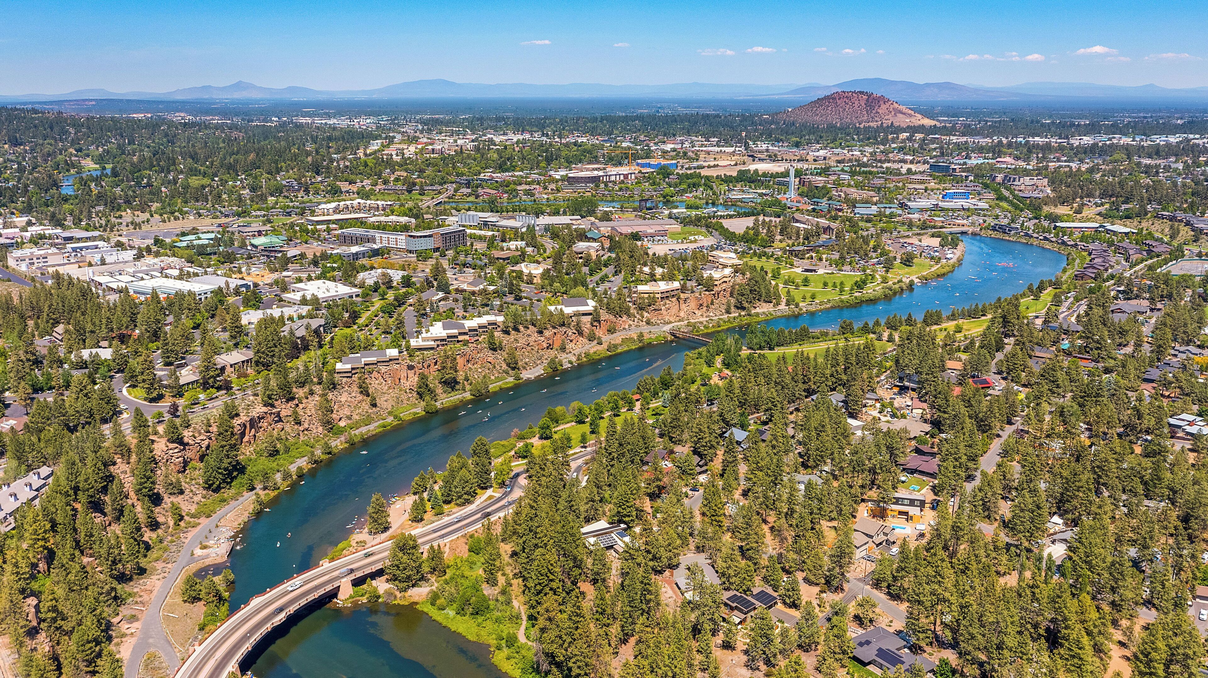An aerial view of a town with a river, residential areas, and a mountain in the background.