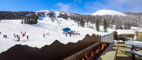 A ski resort with a fire feature, a ski lift, and a snowy mountain backdrop.